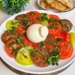 Caprese salad on a plate: colorful tomato slices with burrata cheese in the middle of the plate.