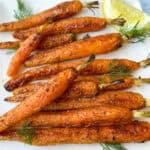 Roasted Dutch carrots on a white plate with a lemon wedge and fresh dill.