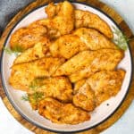 Golden, delicious looking thin chicken breasts are served on a white plate.