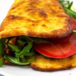 Golden viral cottage cheese wrap served with green salad and sliced tomatoes on a white plate.