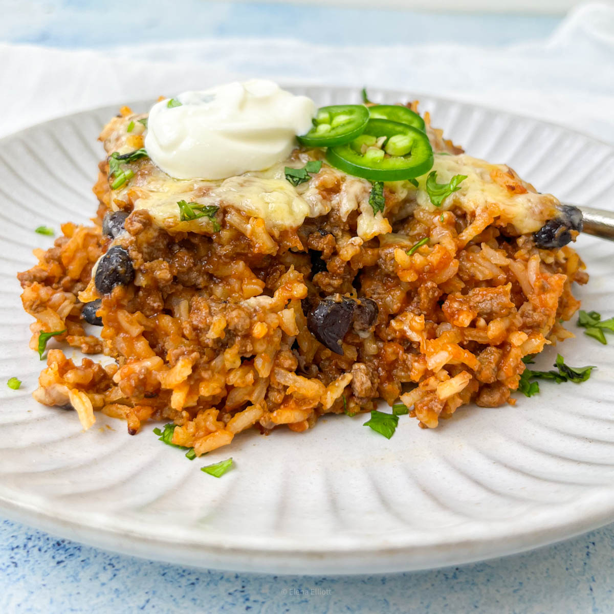 Mexican beef and rice served on a grey plate with a dollop of yogurt and green chilies.