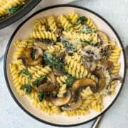Creamy pasta with wilted spinach and golden mushroom slices on a white plate served with grated parmesan cheese.